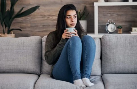 depression sad and woman with coffee on a sofa for thinking lonely and isolated in a living room